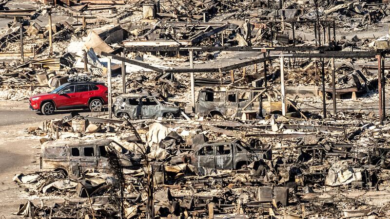 A car drives past homes and vehicles destroyed by the Palisades Fire at the Pacific Palisades...