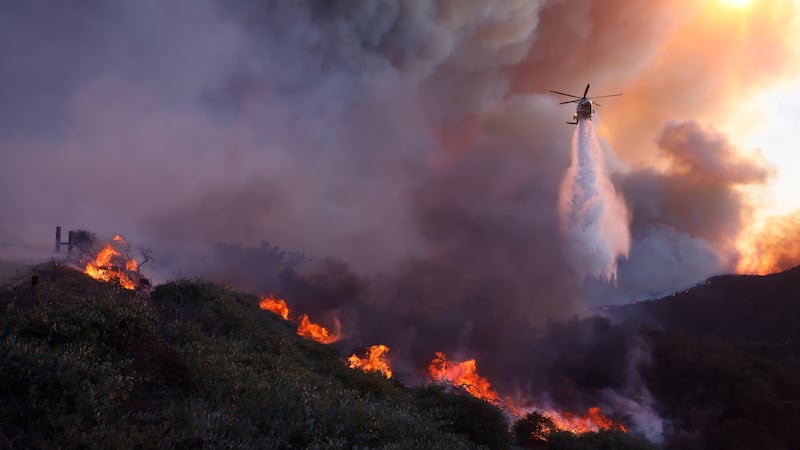 Water is dropped by helicopter on the advancing Palisades Fire in the Pacific Palisades...
