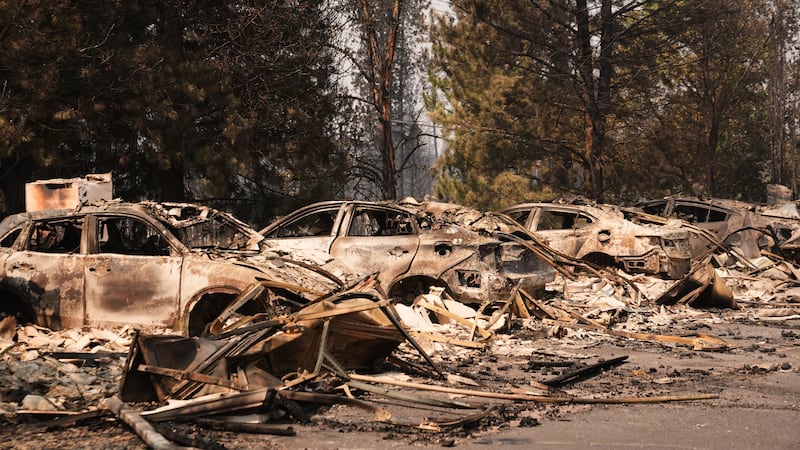 A line of burned cars sit in a parking lot Tuesday, Aug. 4, 2026, after a wildfire hit the...
